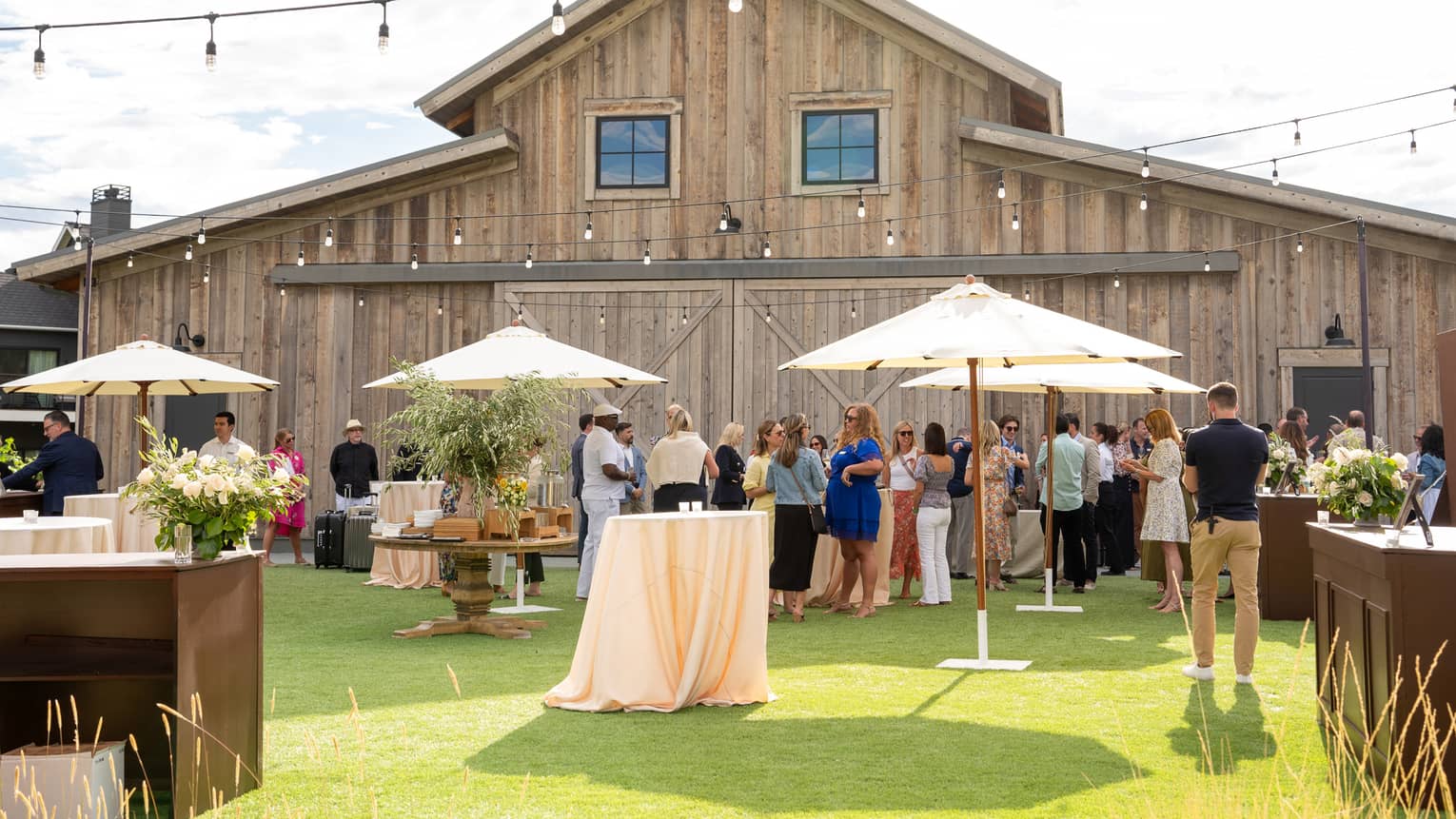 A vineyard barn with lights hung above and umbrellas near standing tables