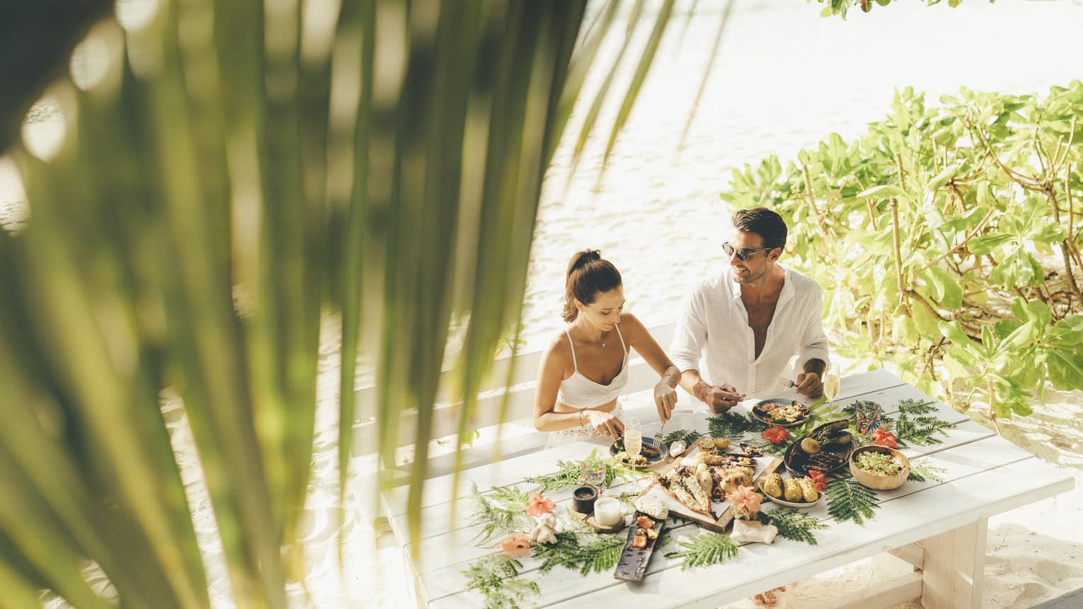 A man and a woman savour a meal on the beach at the Steak Shack beachside island grill.