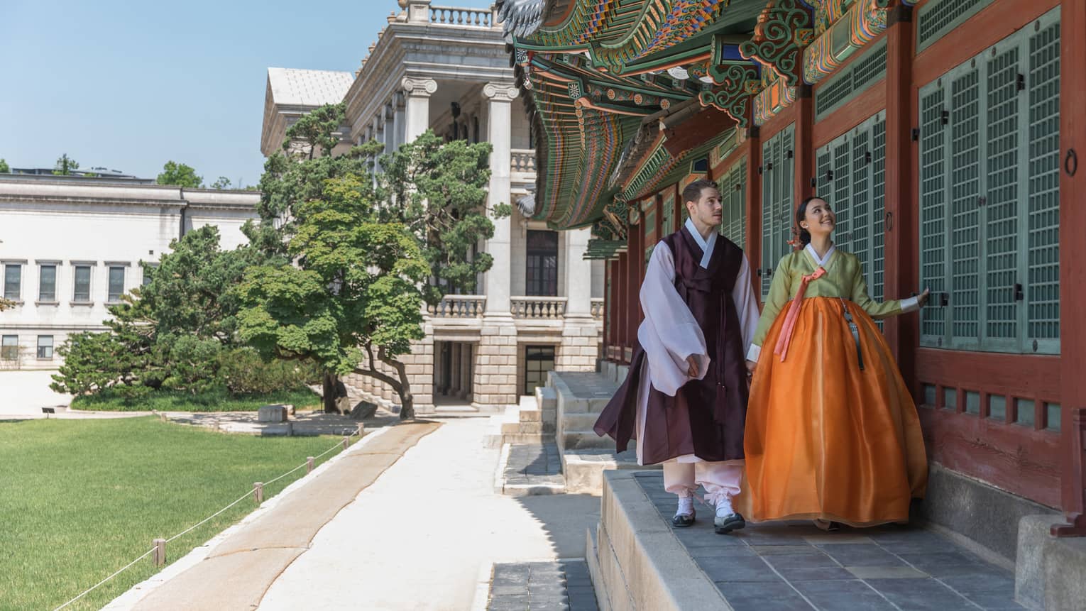 Man and woman in traditional Korean attire walk along the wall of a local palace