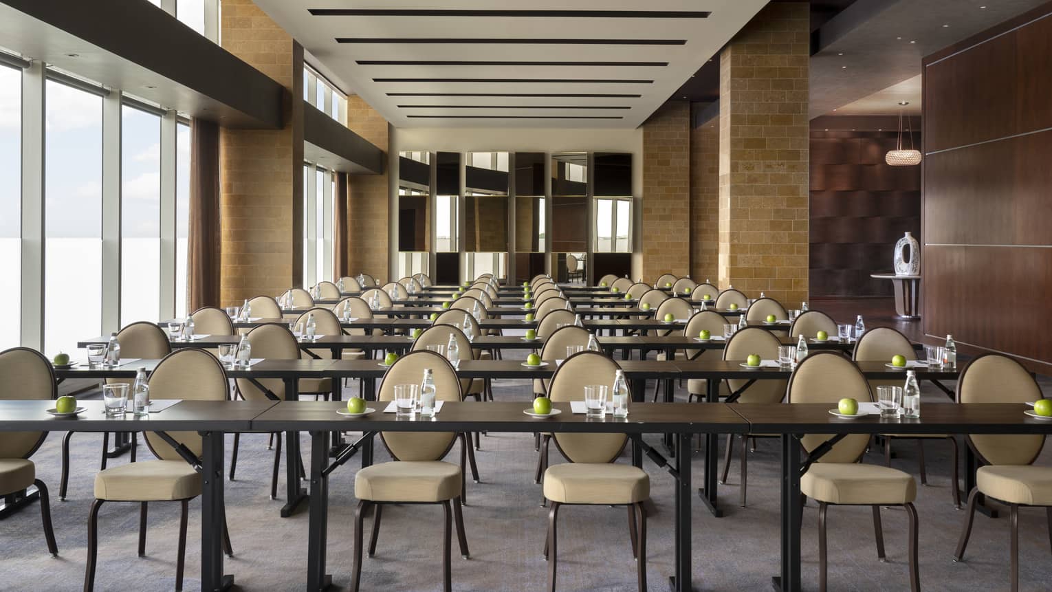 A large meeting room with rows of tables and chairs and large windows.