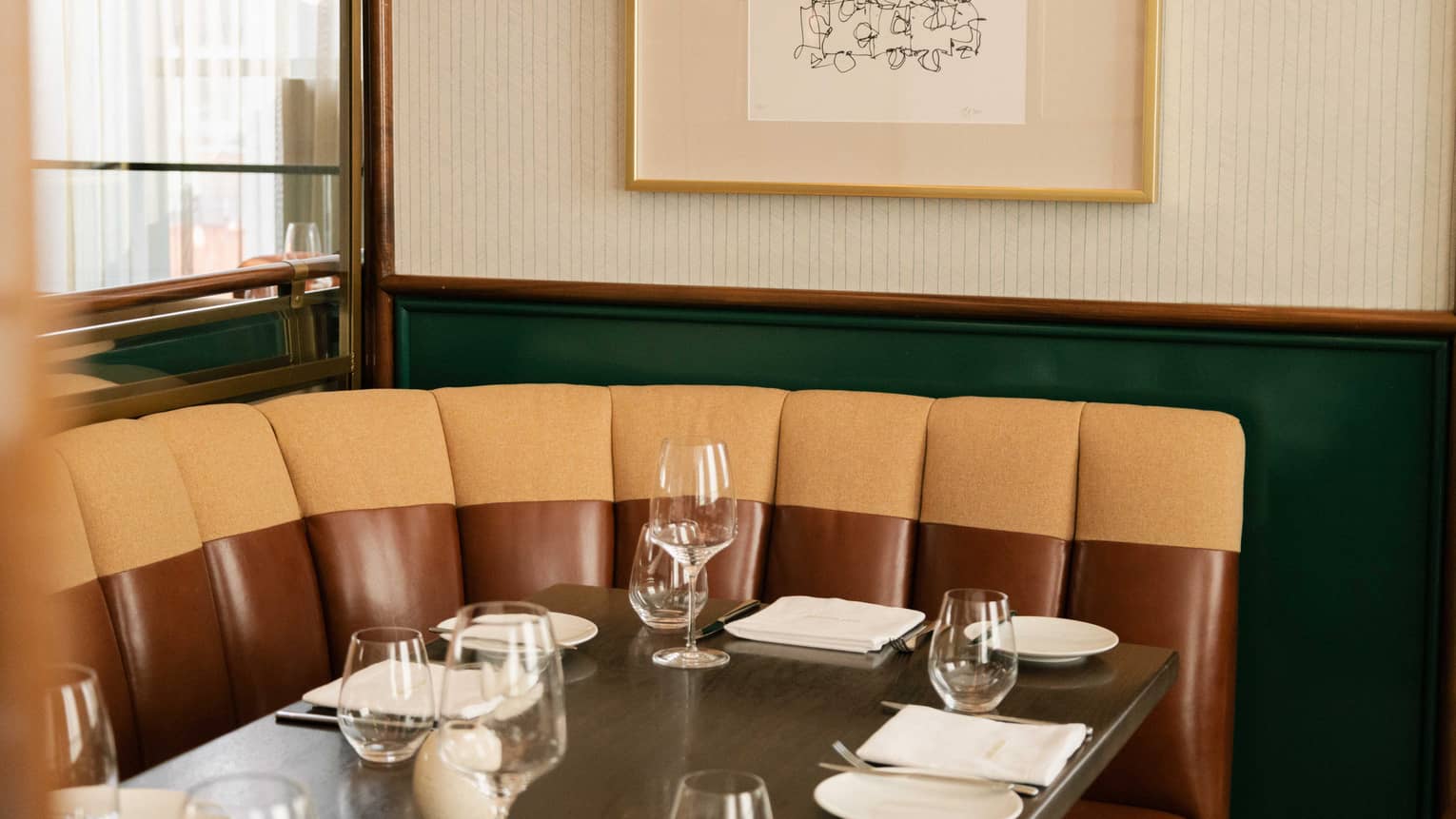 Close up view of a corner booth and table topped with wine glasses and white plates below a framed art print