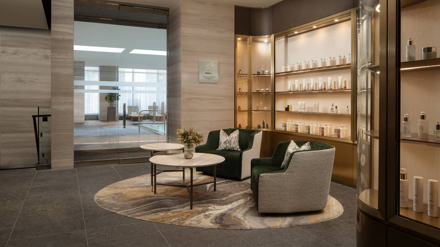 Spa reception area with olive green armchairs and round nesting coffee tables, rows of spa products on wall
