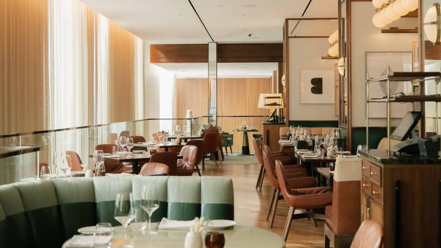 The interior of a softly lit restaurant with floor-to-ceiling curtains on one side of the room.