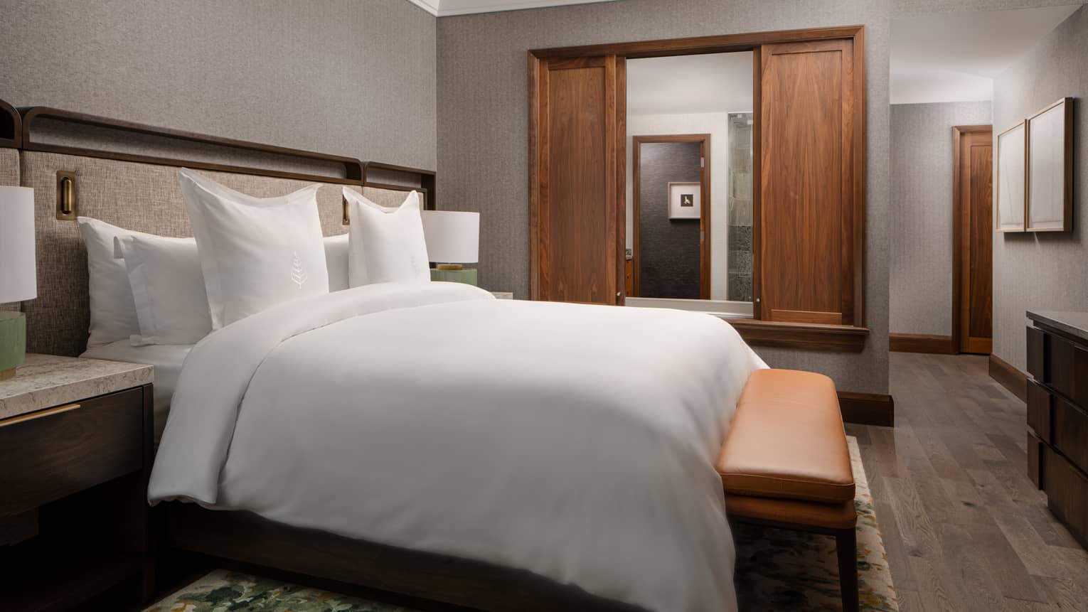 Bedroom with king bed, bench, sliding wooden doors to bathroom