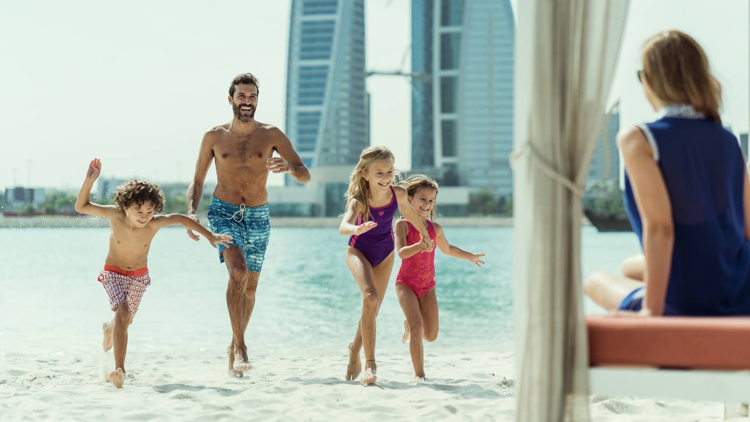 A small family runs across the beach towards a beachside cabana.