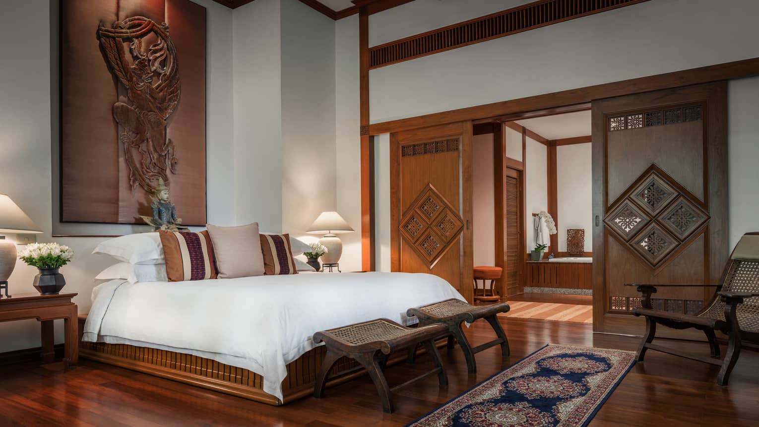 Spacious bedroom with a large bed, wooden furniture, carved sliding doors, decorative cushions and traditional artwork on the wall