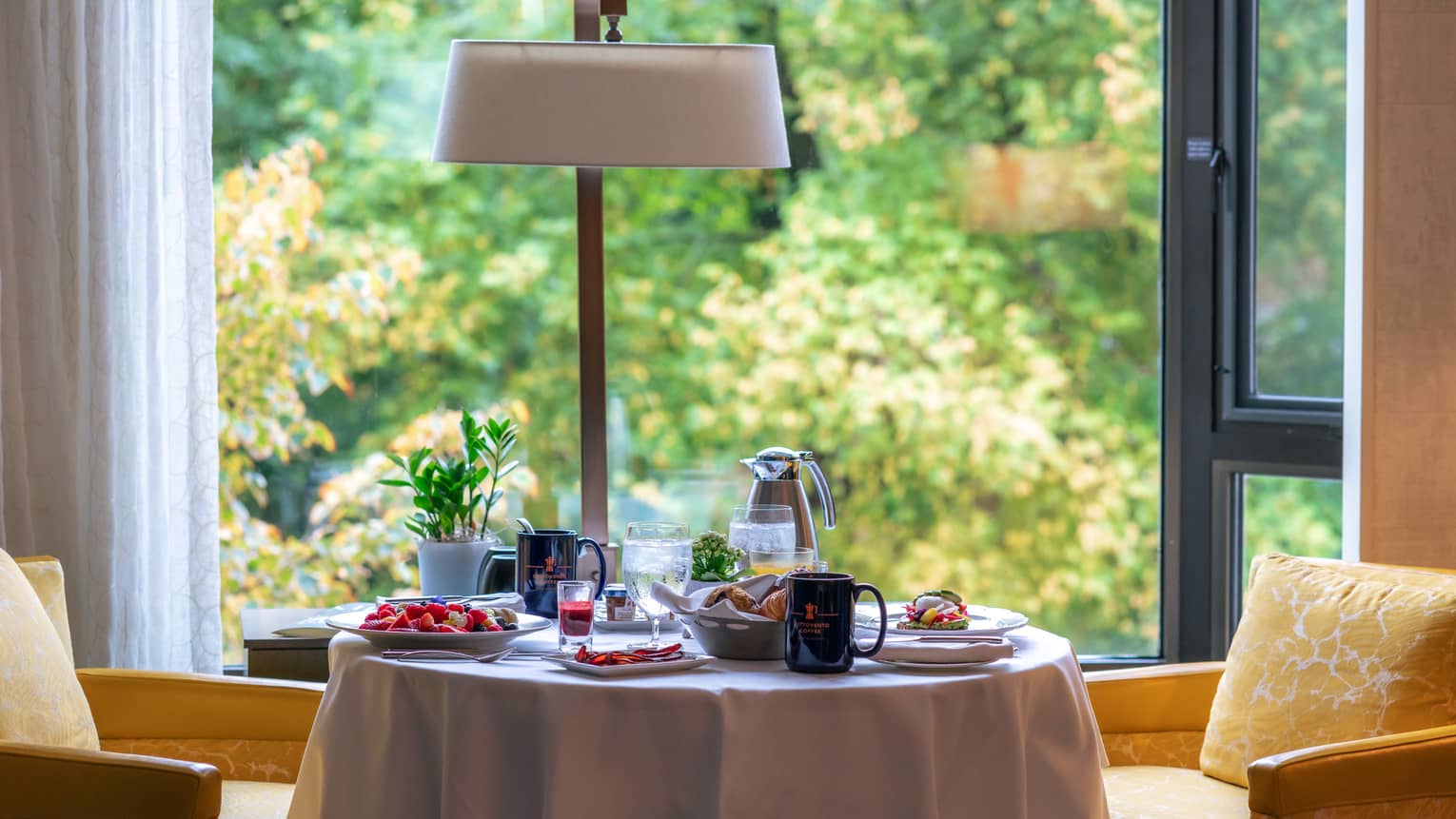 A dining table with yellow chairs beside a window view of trees