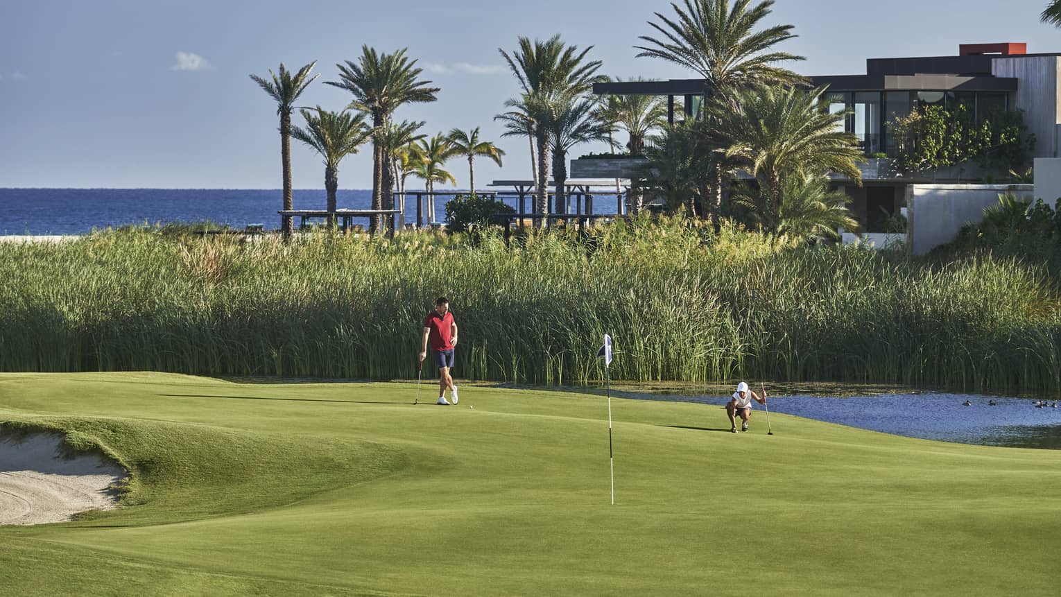 Two golfers enjoy a day on the golf course at four seasons Los Cabos with palm trees and the ocean in the background