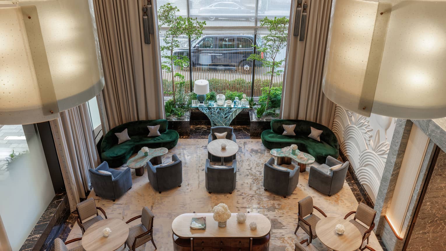 A view from above of a bright, airy open lounge area with comfortable seating, large windows, tables and elegant neutral-toned decor