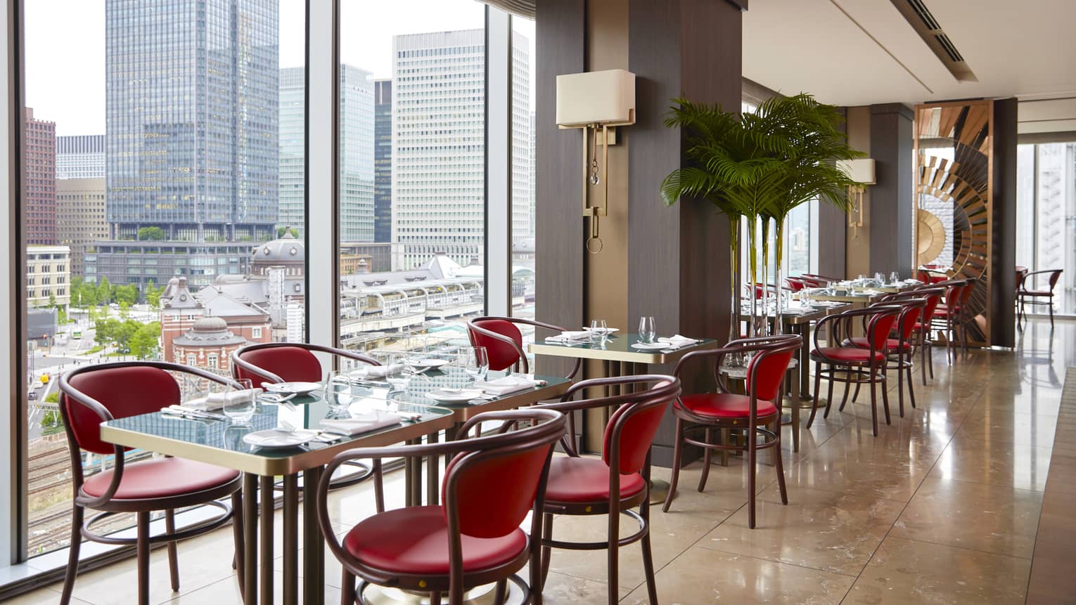 Row of four tables with four chairs each at Maison Marunouchi, floor-to-ceiling windows with views of downtown Tokyo