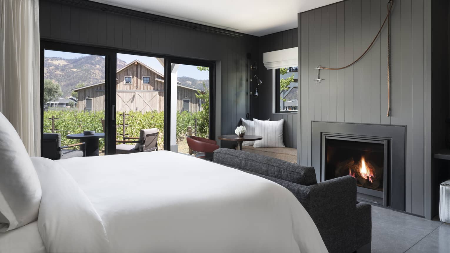 Luxury resort room with a king bed, cozy fireplace, vineyard view, seating area and outdoor patio facing rustic barn and mountains