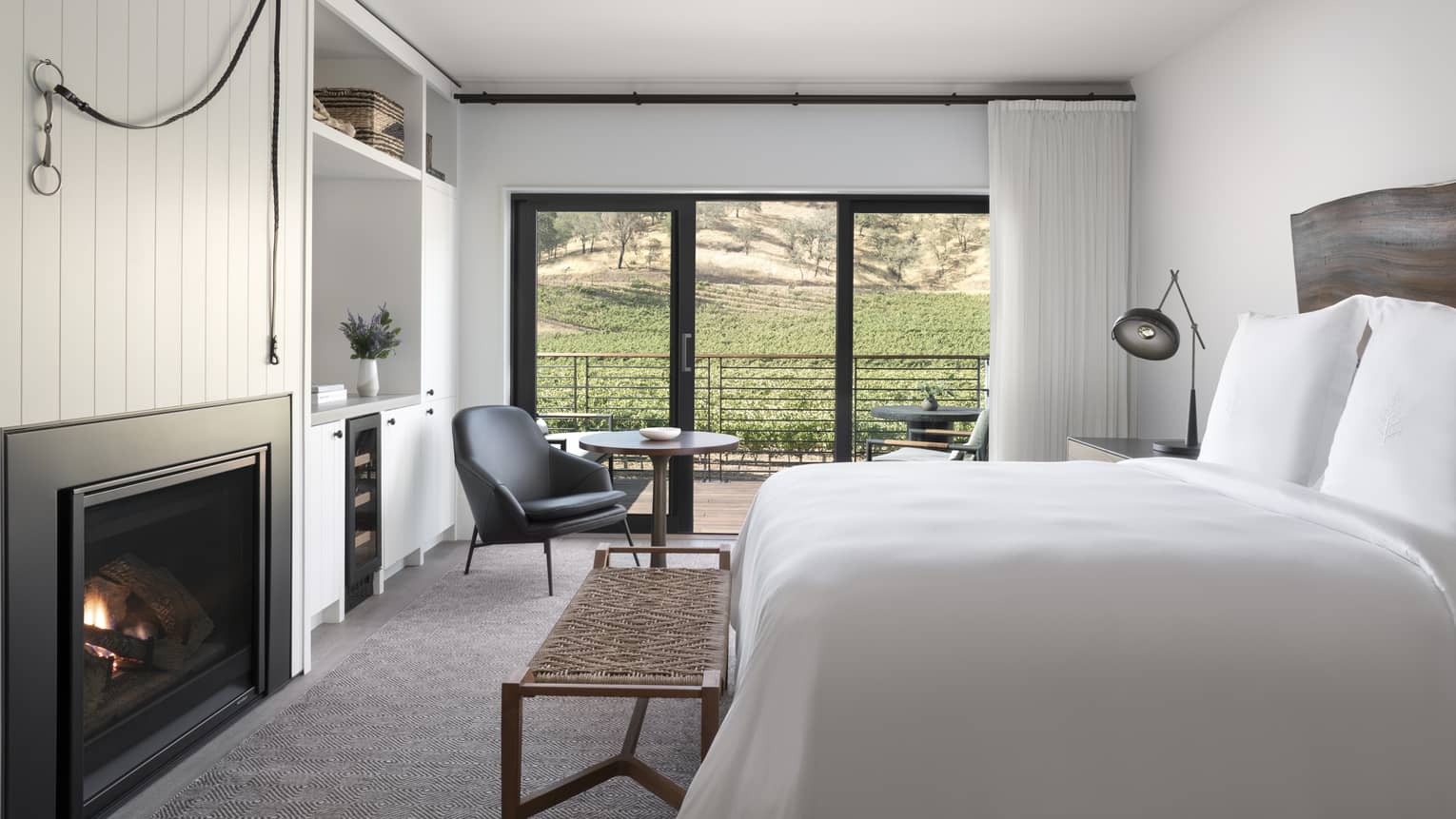 Luxury resort room with a king bed, fireplace, wooden headboard, lounge chair and balcony overlooking vineyard and hillside