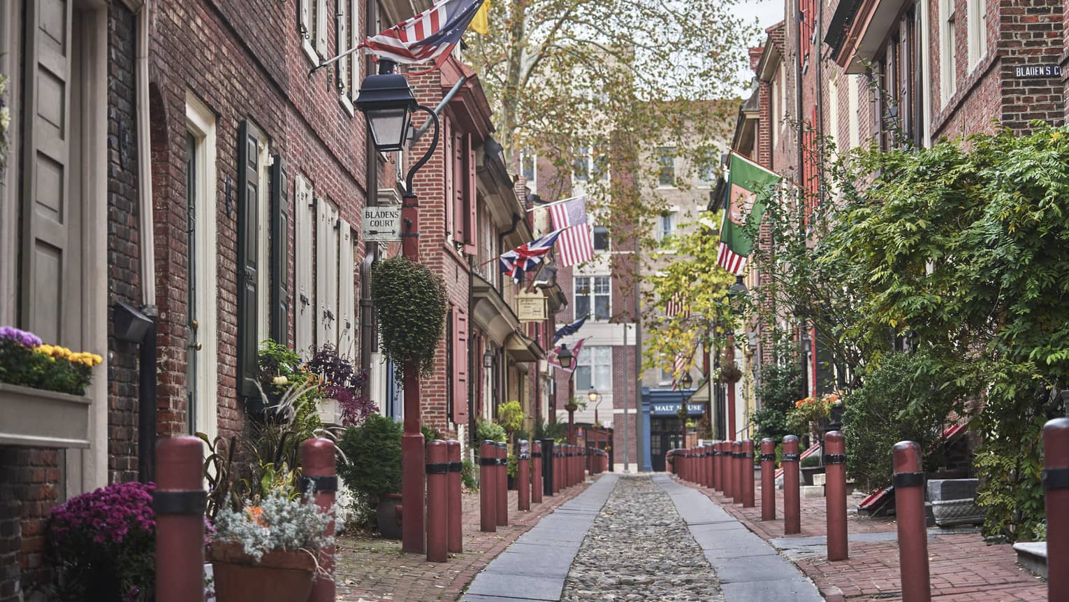 An old cobble-stone street lined with charming brick buildings, plants and patriotic flags