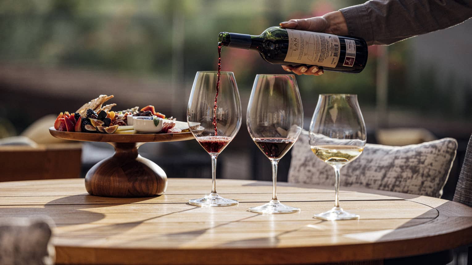 Person pouring wine into three glasses, with a tray of food also on the table.