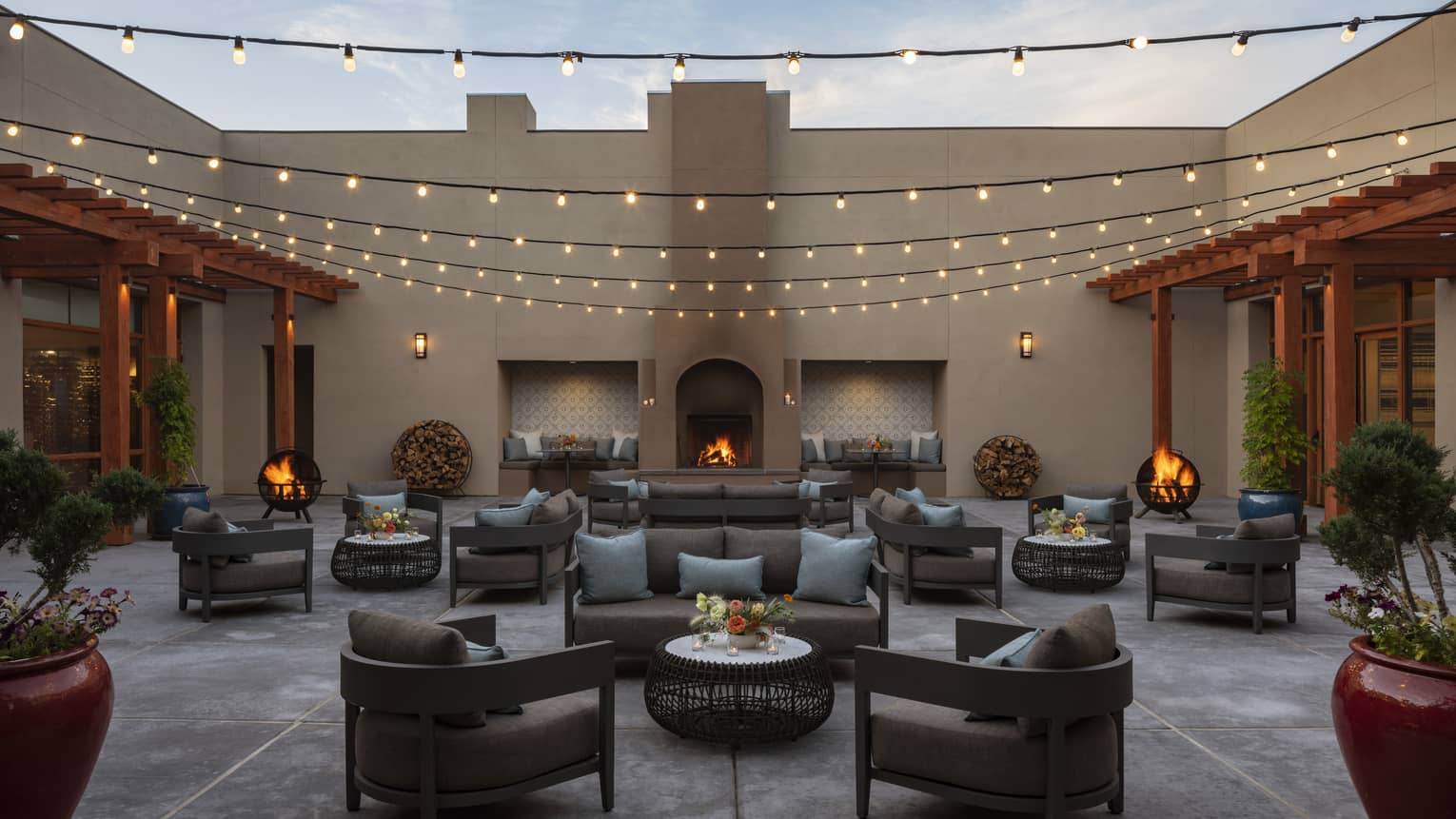 A courtyard area outside with many seats and small tables with fair lights hanging under an open sky.