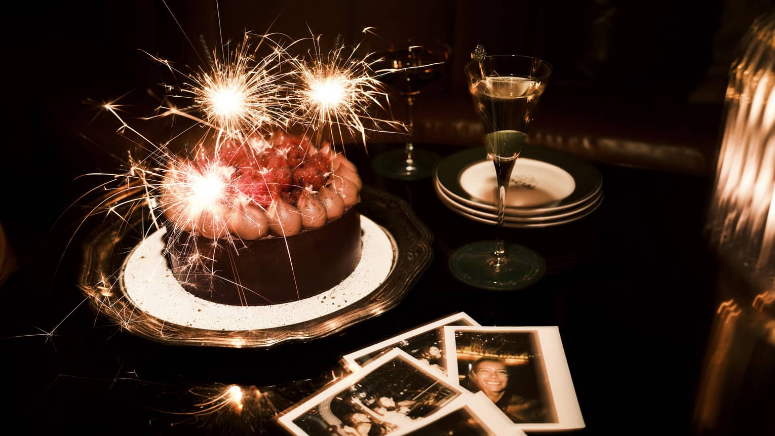 Sparkler candles in a chocolate cake and polaroid pictures nearby on a table