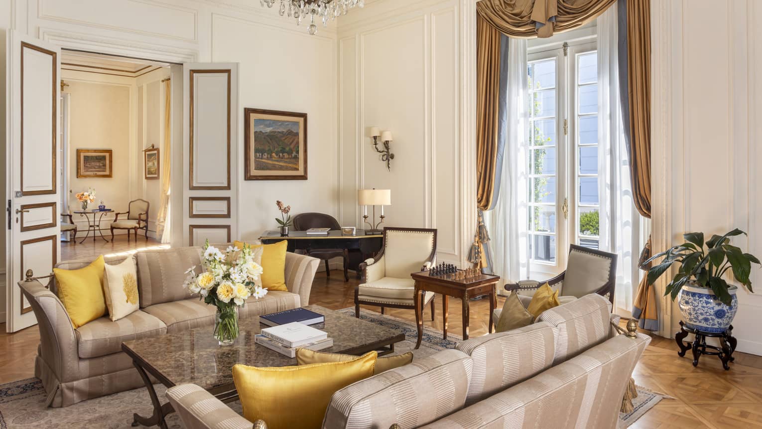 Suite living room with tall ceilings, set of French doors, two sofas facing each other and various tables