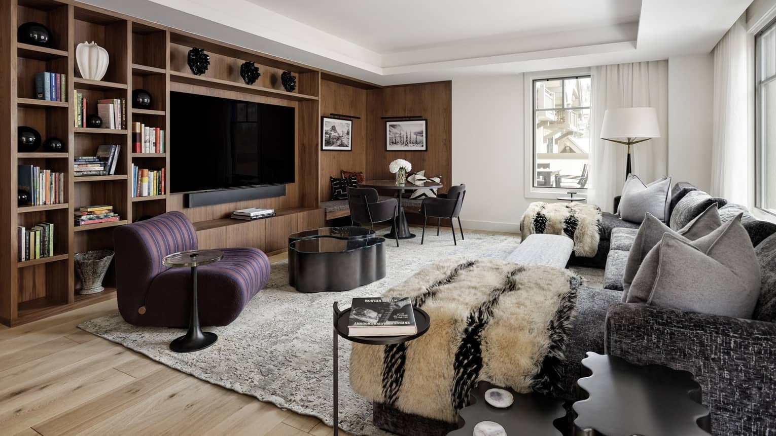 Contemporary living room of a private residence rental, featuring a grey sofa, plum-coloured arm chair and built-in media centre