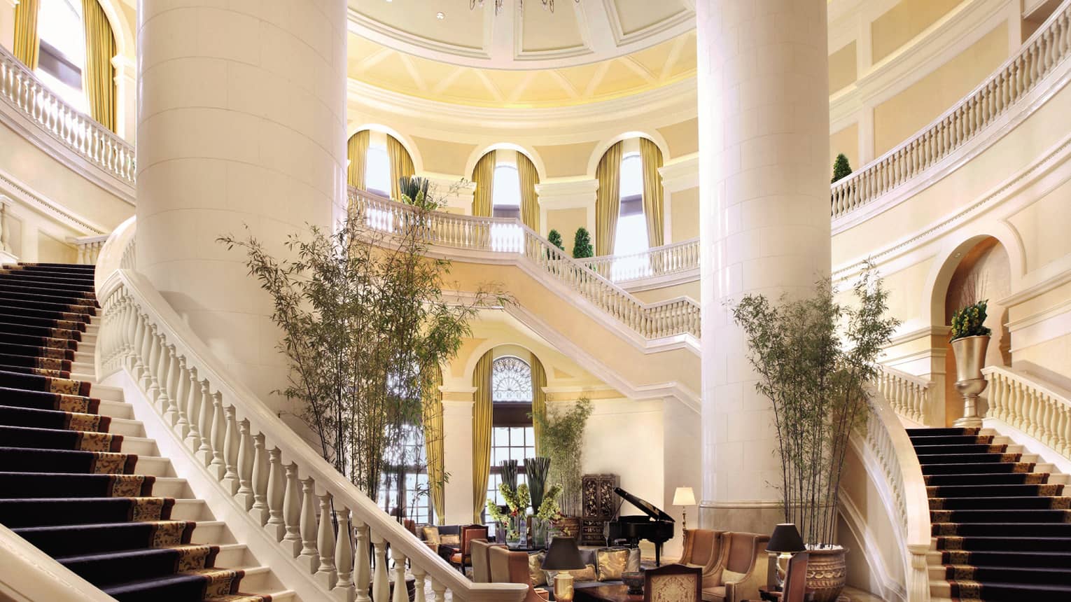 Hotel lobby with two grand staircases around large white pillars, seating area