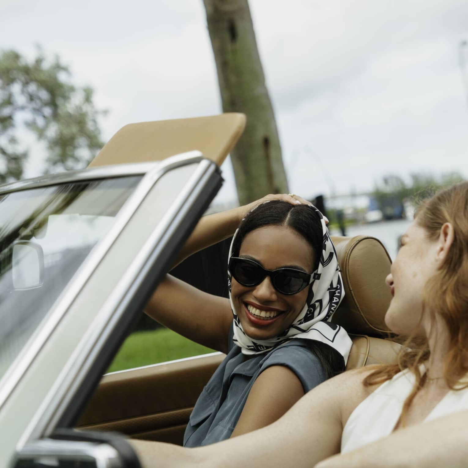 Two guests riding in a convertible car while smiling at one another.