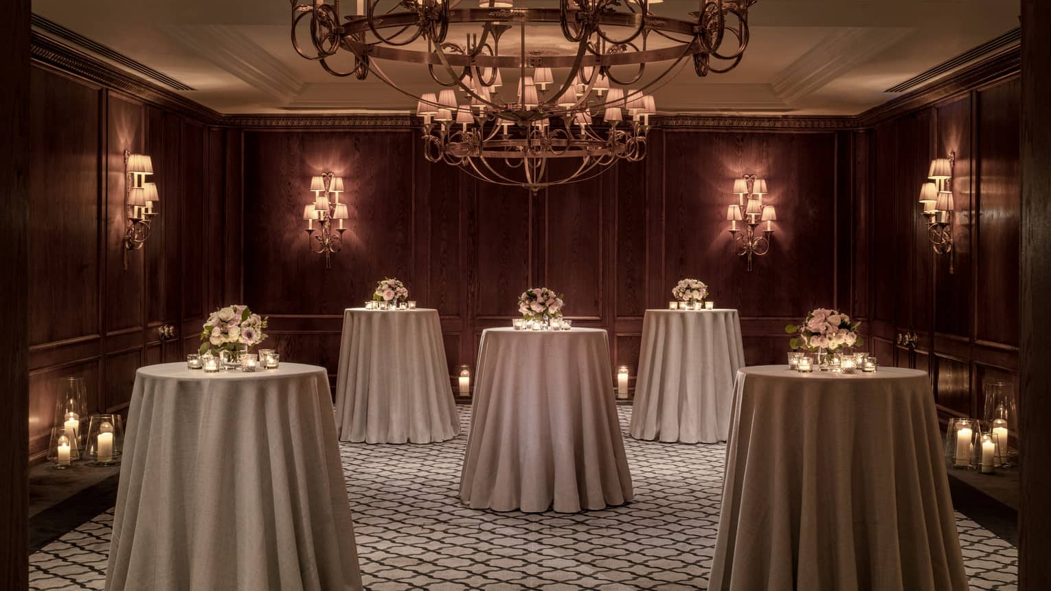 A room with standing round tables and a chandelier.