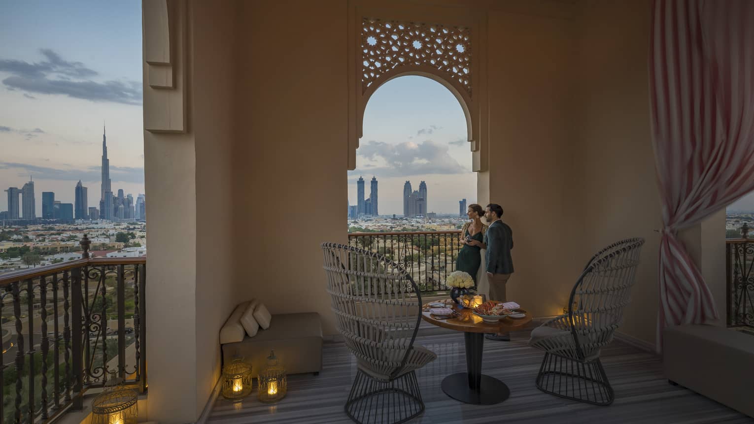 A man and woman lean against a wall of an outdoor terrace an peer through an opening, over the city in Dubai at Jumeirah Beach