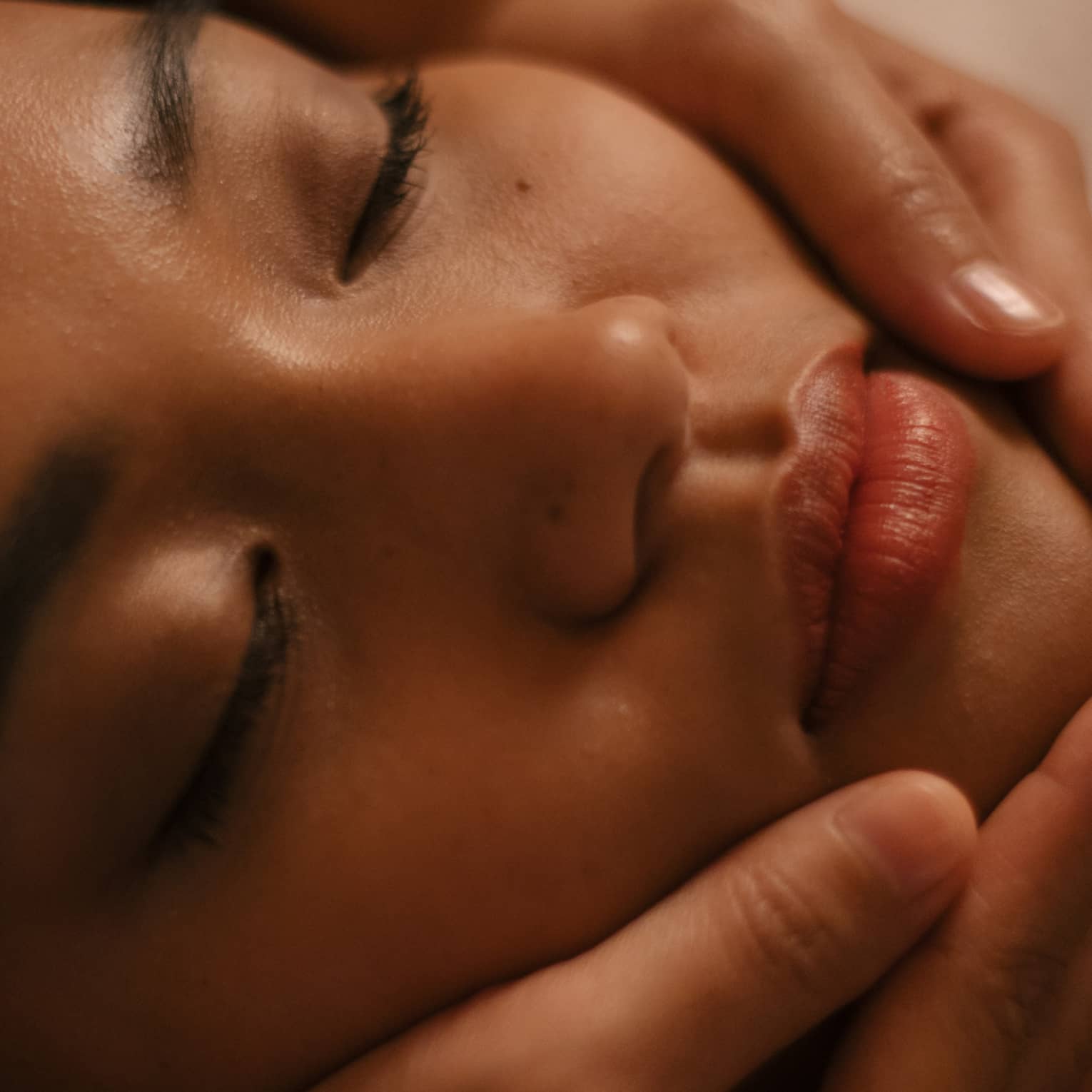 Closeup of hands on either side of woman’s face during facial
