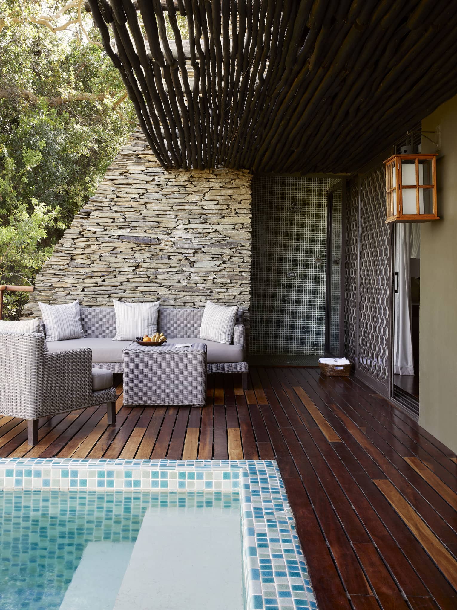 Terrace with pool corner in view, wood-slatted deck, neutral seating vignette against stacked stone wall and sliding doors to right