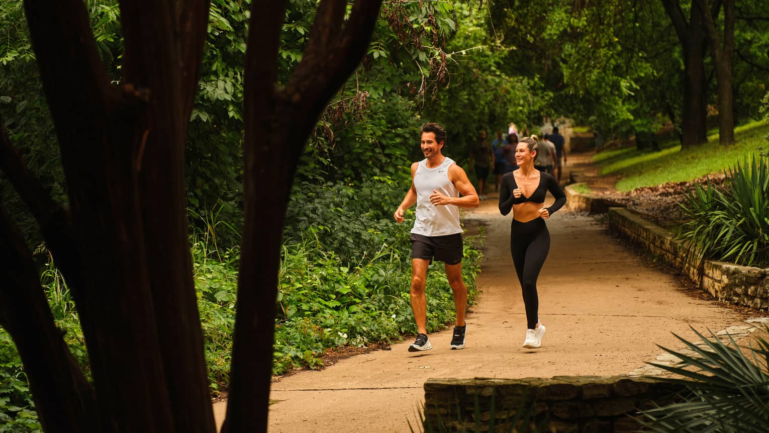 Two guests running together on an outdoor trail surrounded by trees