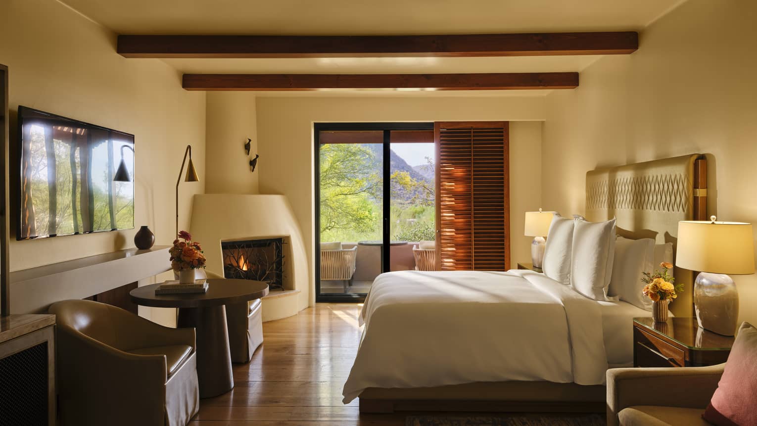 Light streams into a luxury bedroom featuring king bed, kiva fireplace, walk-out terrace and beamed ceiling