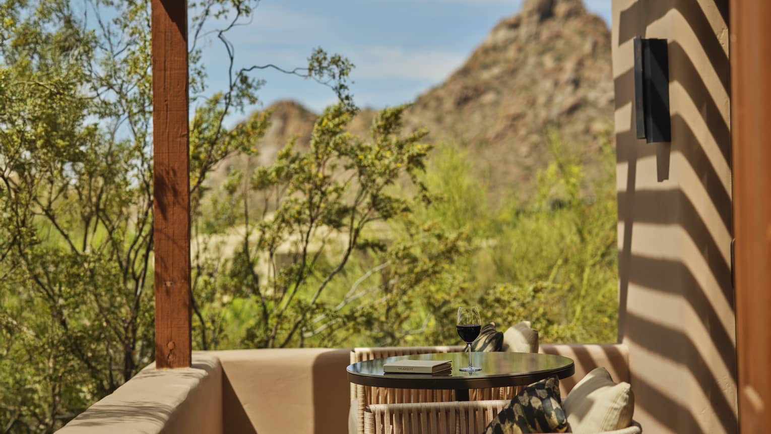 A sunny private terrace with wooden pergola, table with two chairs, and views of the desert