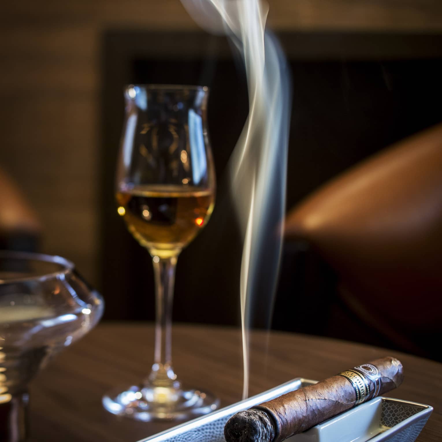 Smoking cigar on tray under glass with liquor