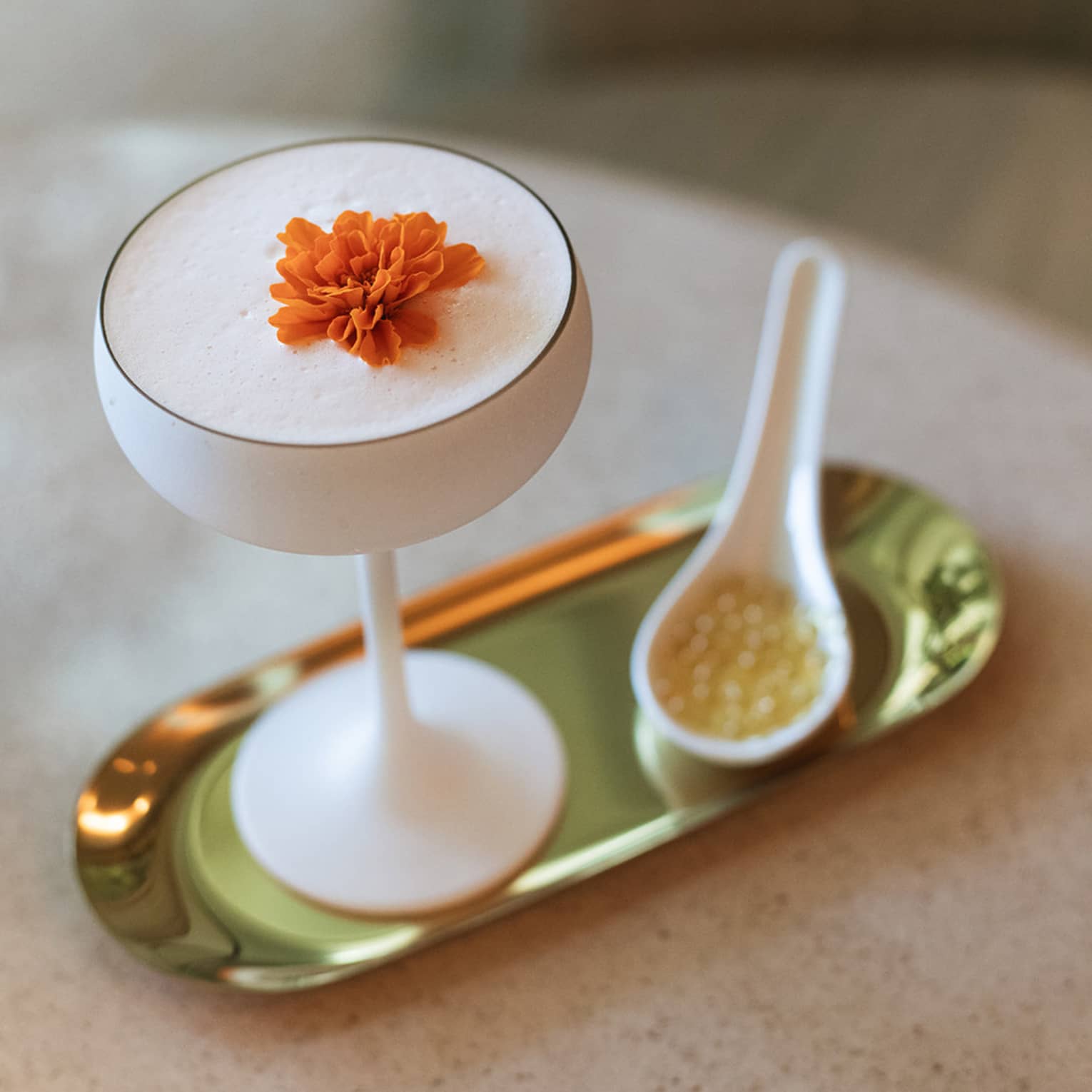 White opaque coupe glass filled with a cocktail and topped with an orange flower