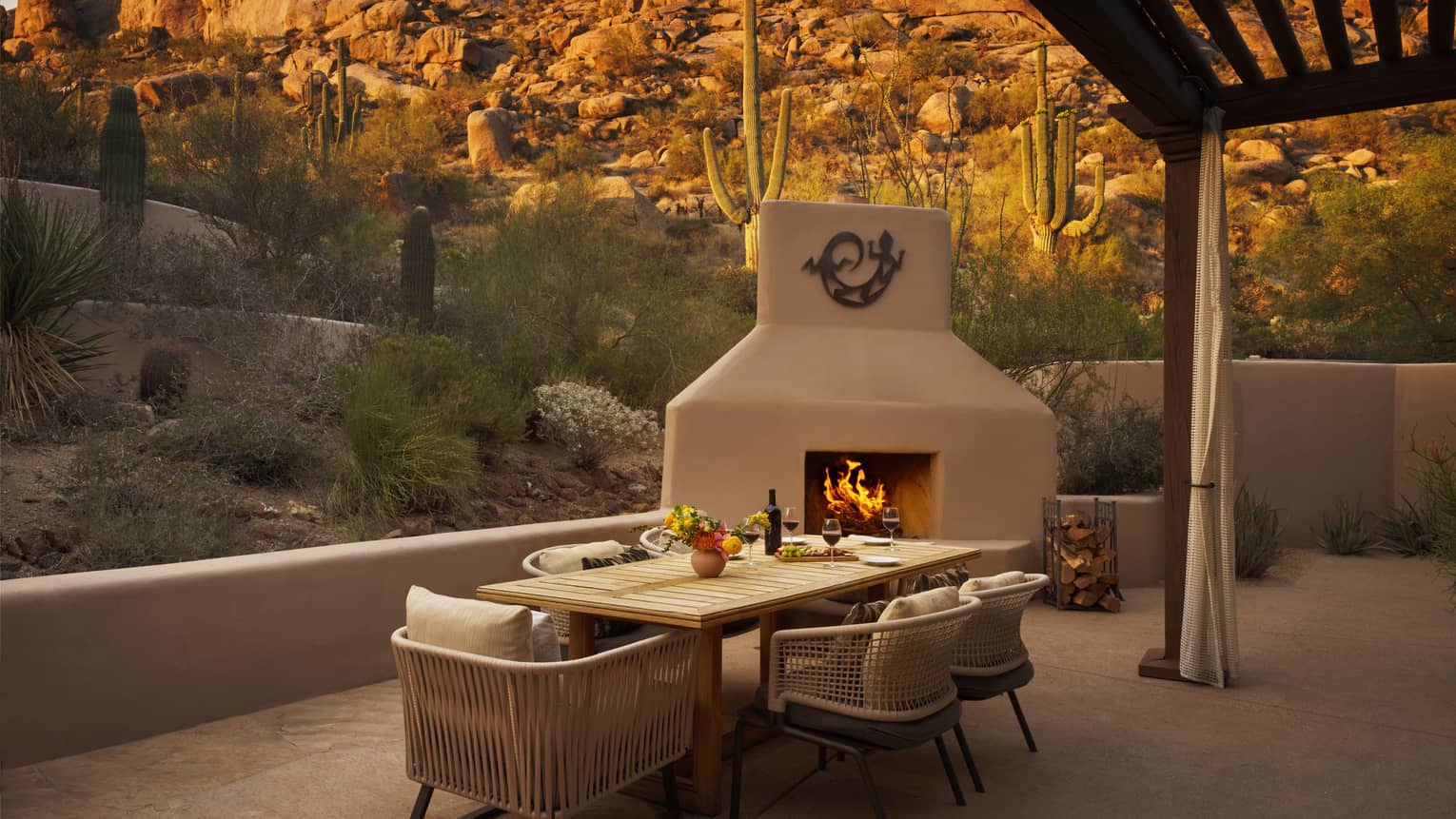 Private terrace of a resort suite, featuring a contemporary dining table, outdoor fireplace and views of the desert and rocky mountain