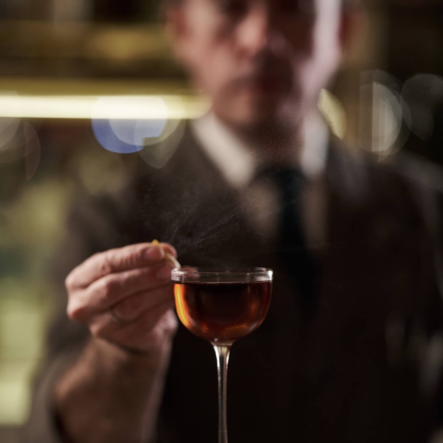 Bartender in suit garnishing a tall amber-coloured cocktail