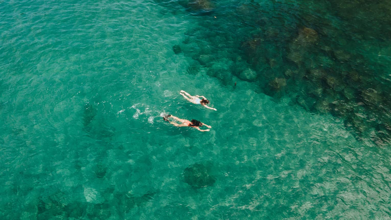 Aerial view of two people snorkelling through blue-green water