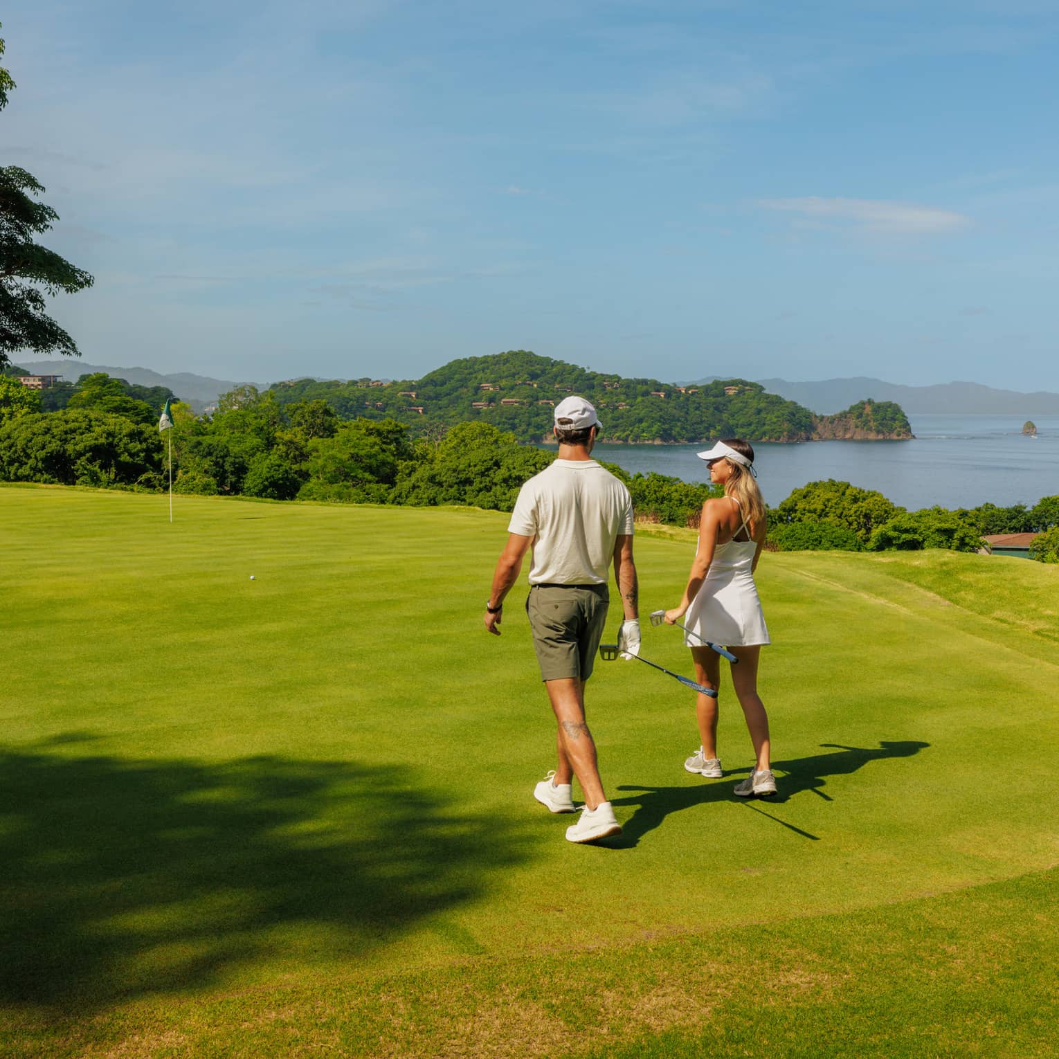 Two golfers walk side by side along a greenway with the ocean in the background