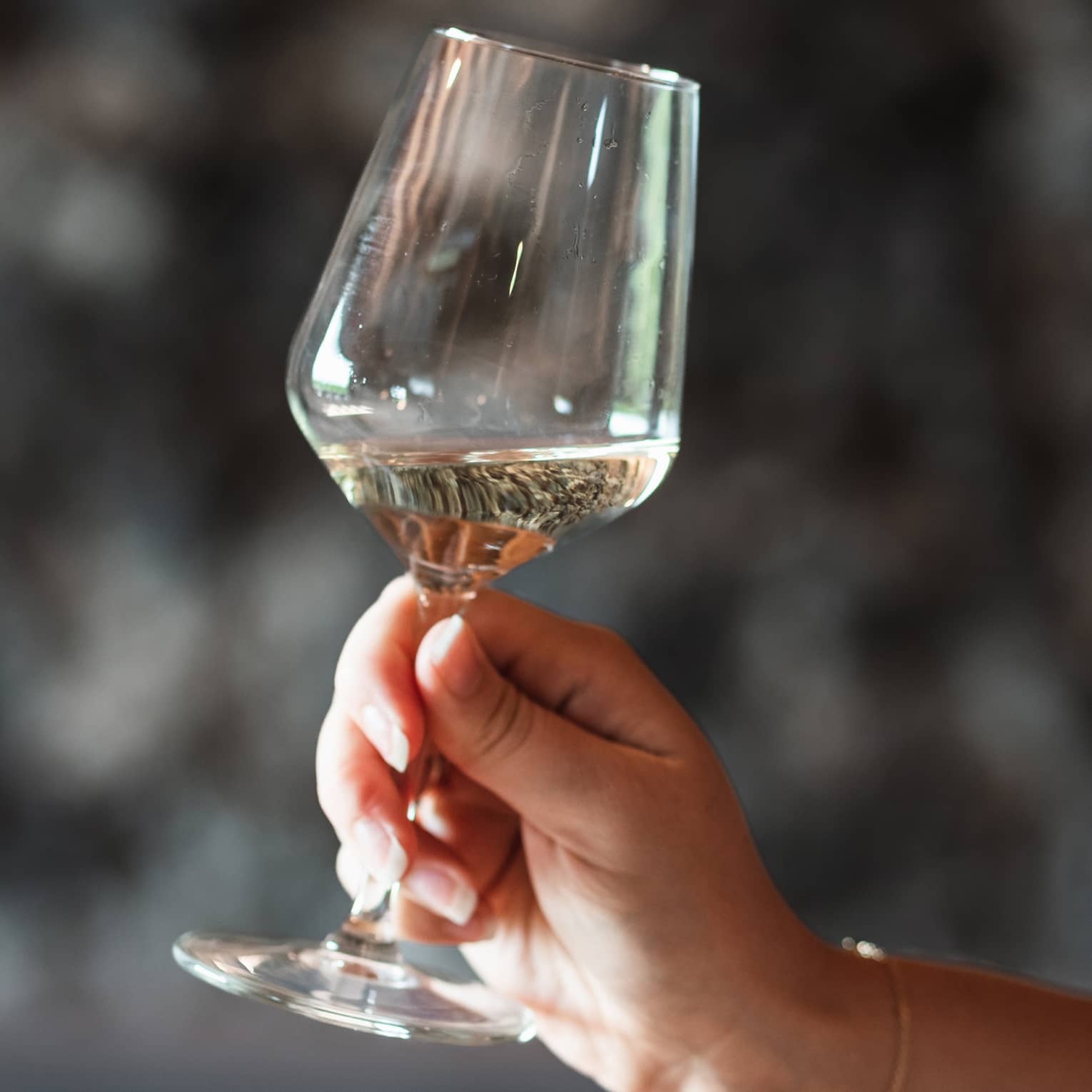 Close-up of a hand holding a tilted glass of white wine against a dark, blurred background.