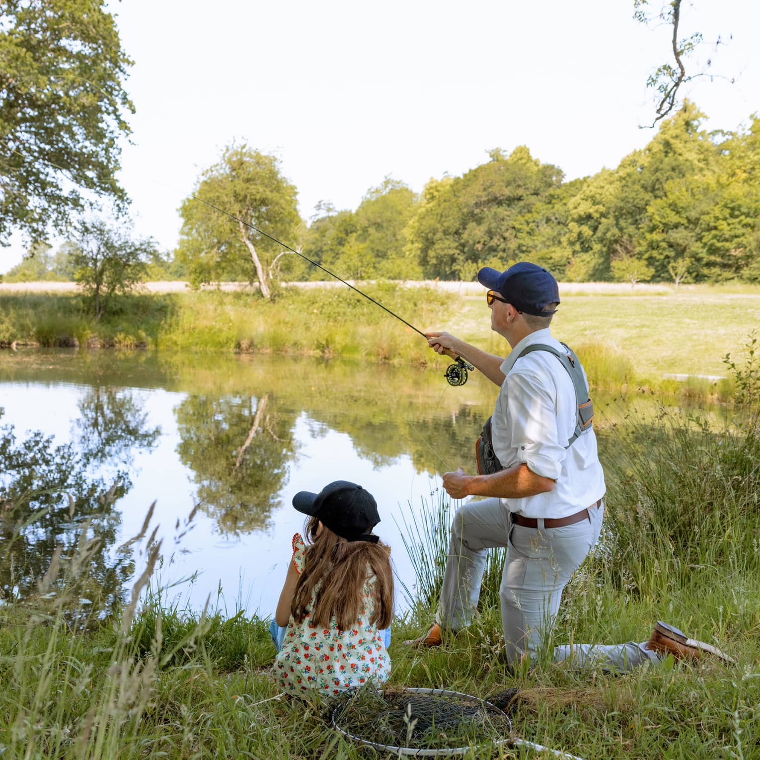 Adult fly fishing at lakeside with child