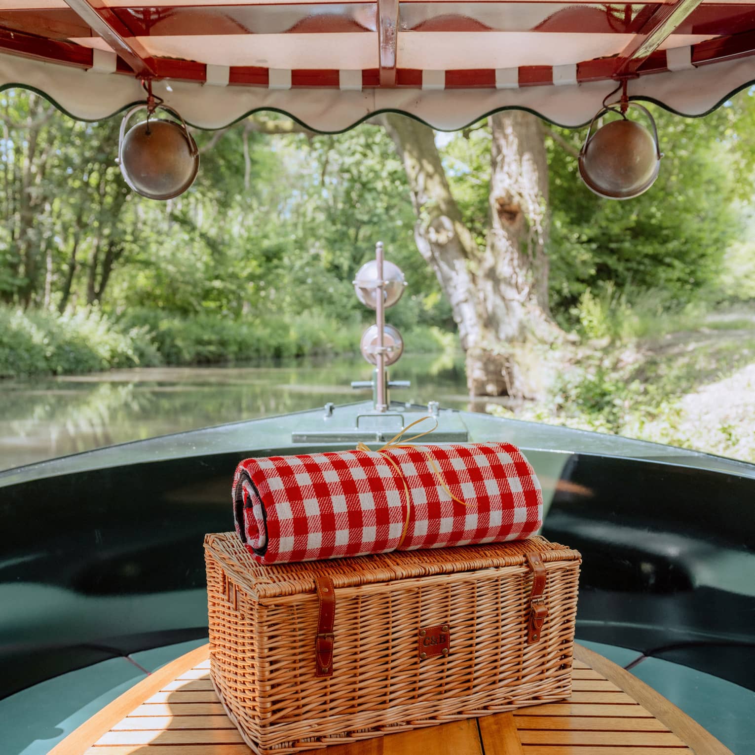 Picnic basket topped with rolled up red gingham blanket inside boat with canvas cover