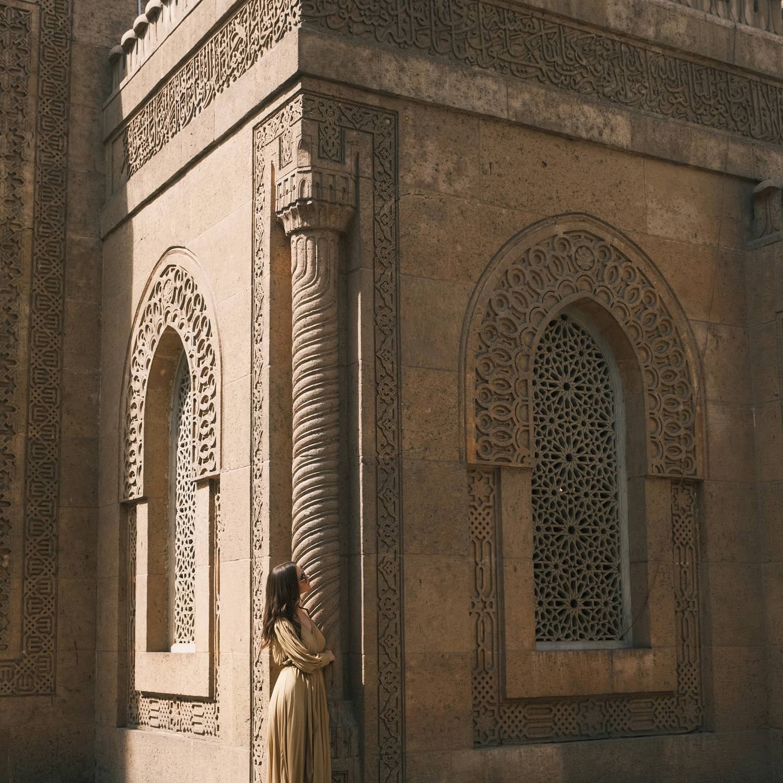 A guest looks up at an ornately carved building featuring a spiral column and arched windows with honeycomb latticework.