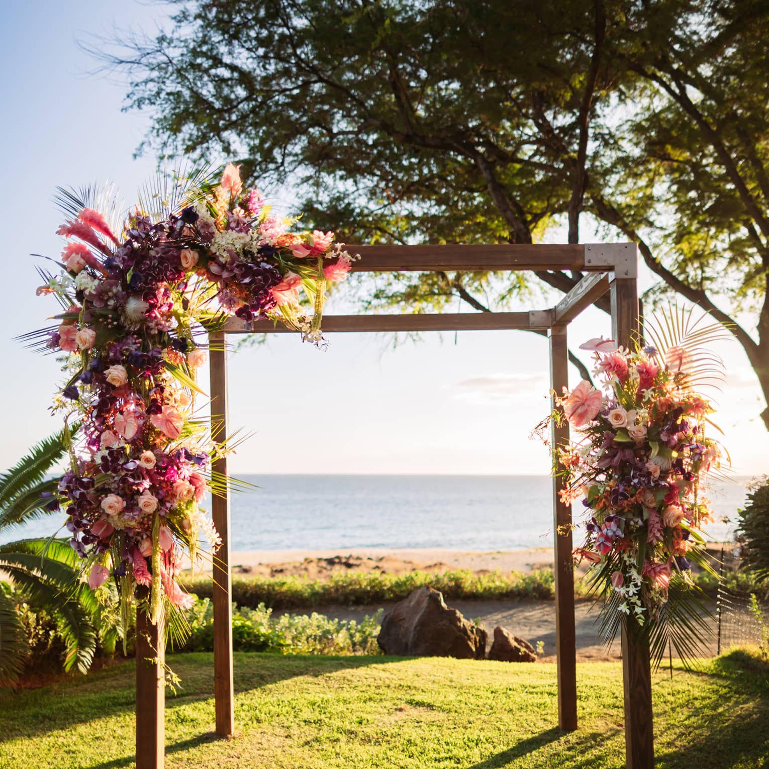 Wooden arch adorned with flowers on Hawaiian lawn, with the ocean in the background
