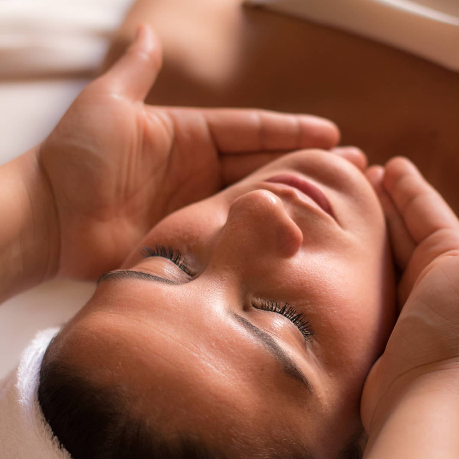 Close-up of woman with eyes closed facing up as hands cup her face and chin