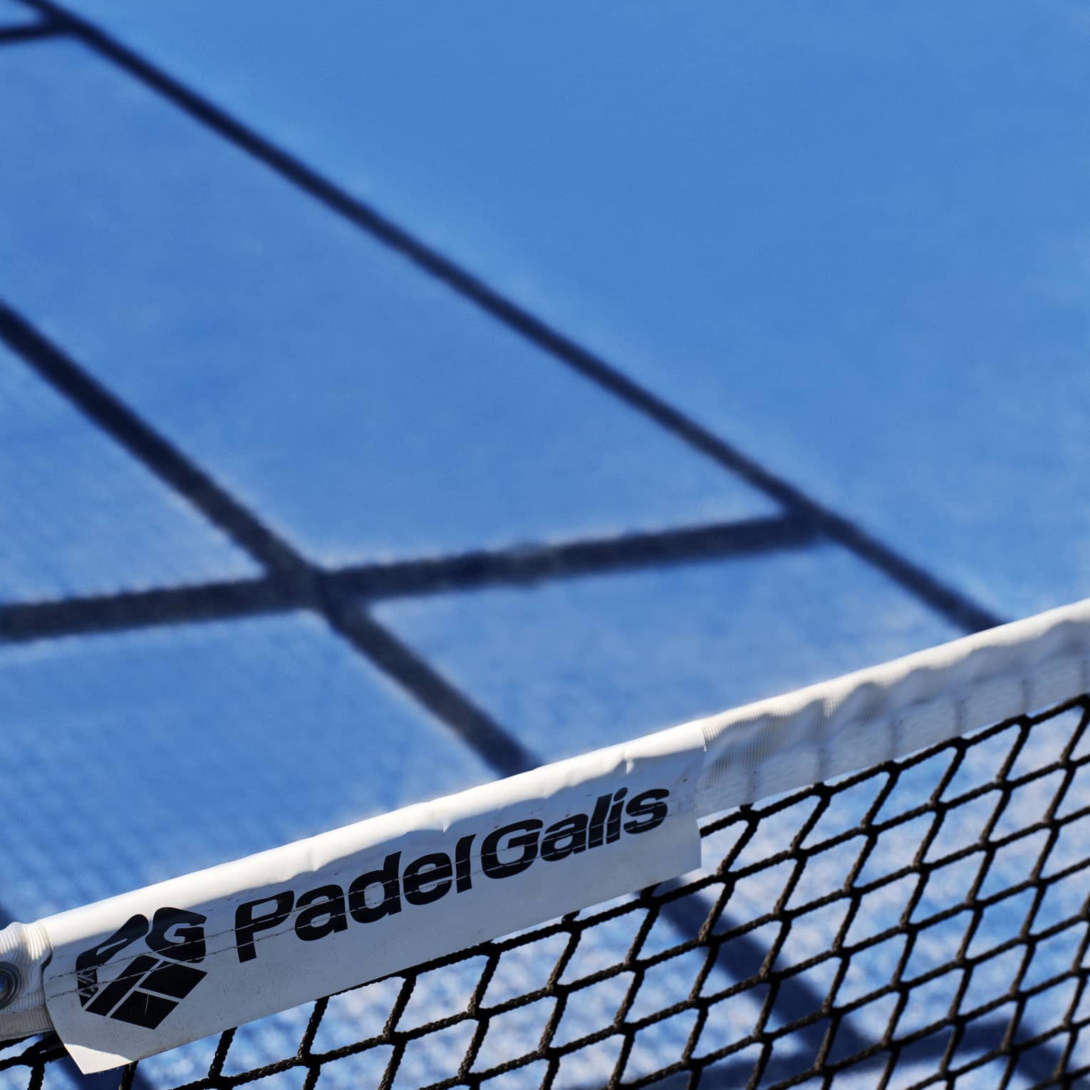 A close-up of the words, Padel Galis, and the company logo on a label of a net on a tennis court.