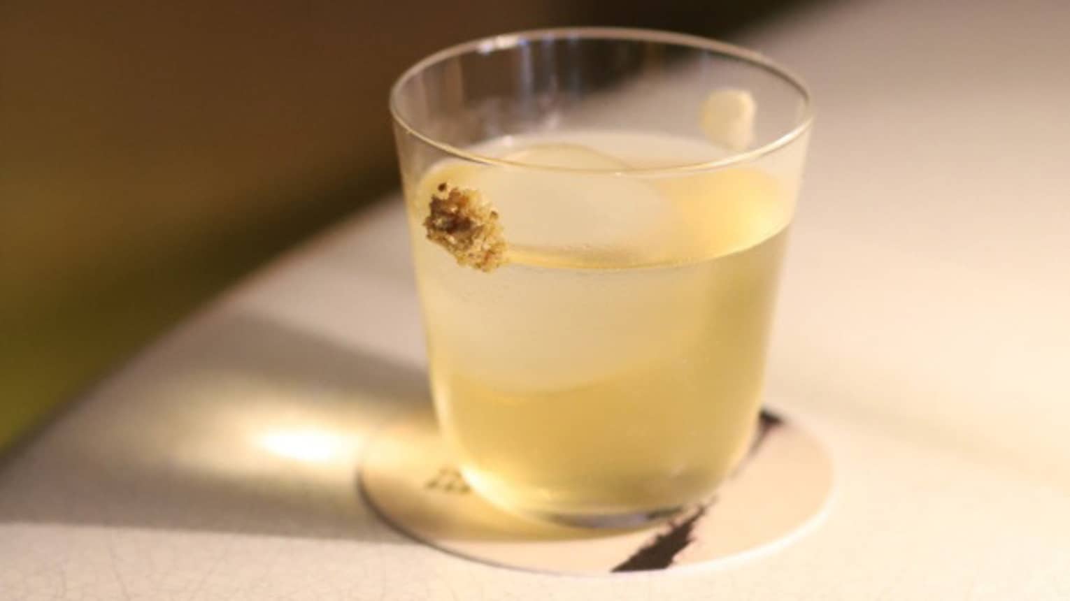 A glass on a coaster with a pineapple flavoured drink in it