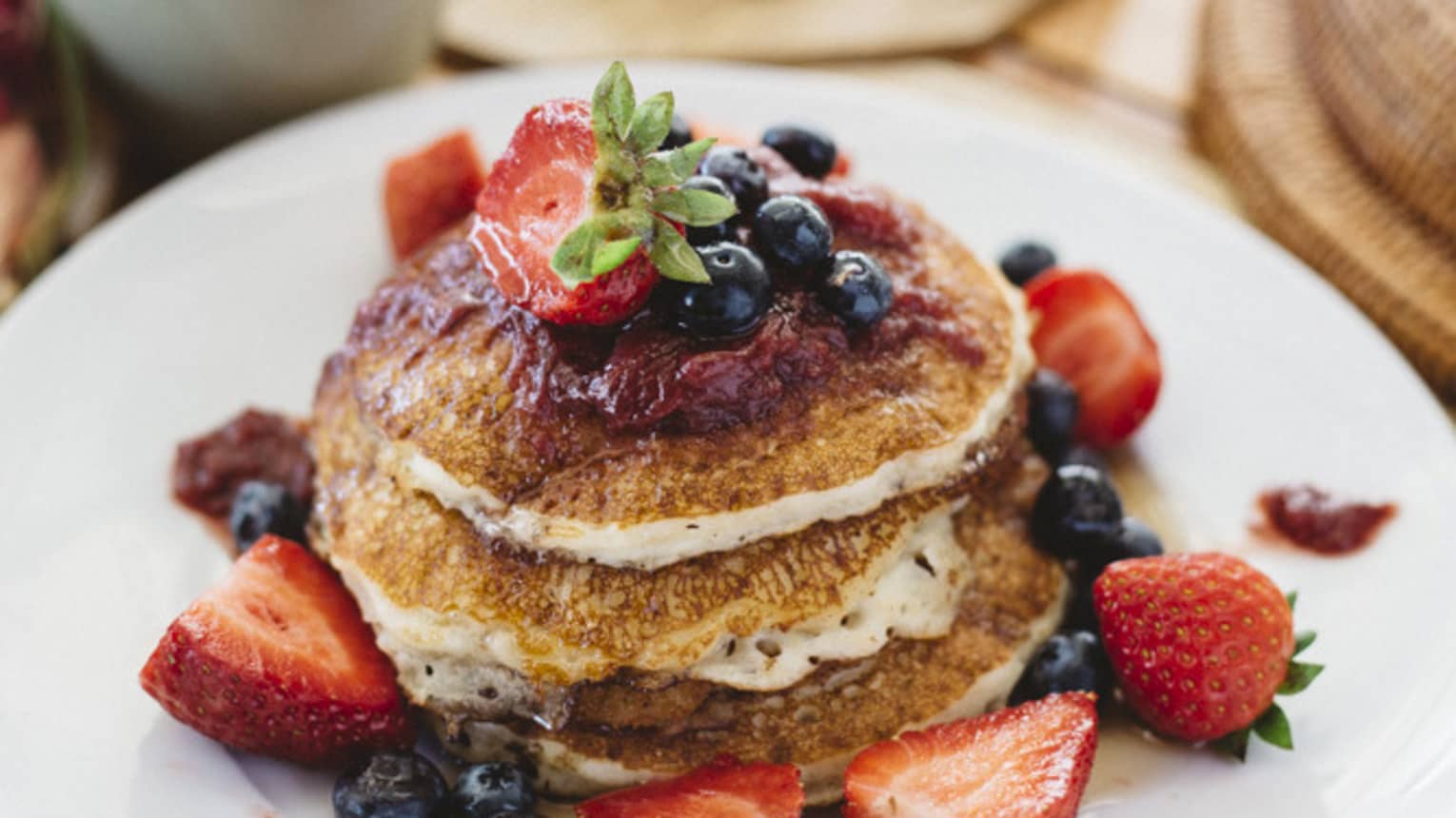 Stack of pancakes topped with strawberries, blueberries, and berry compote on a white plate