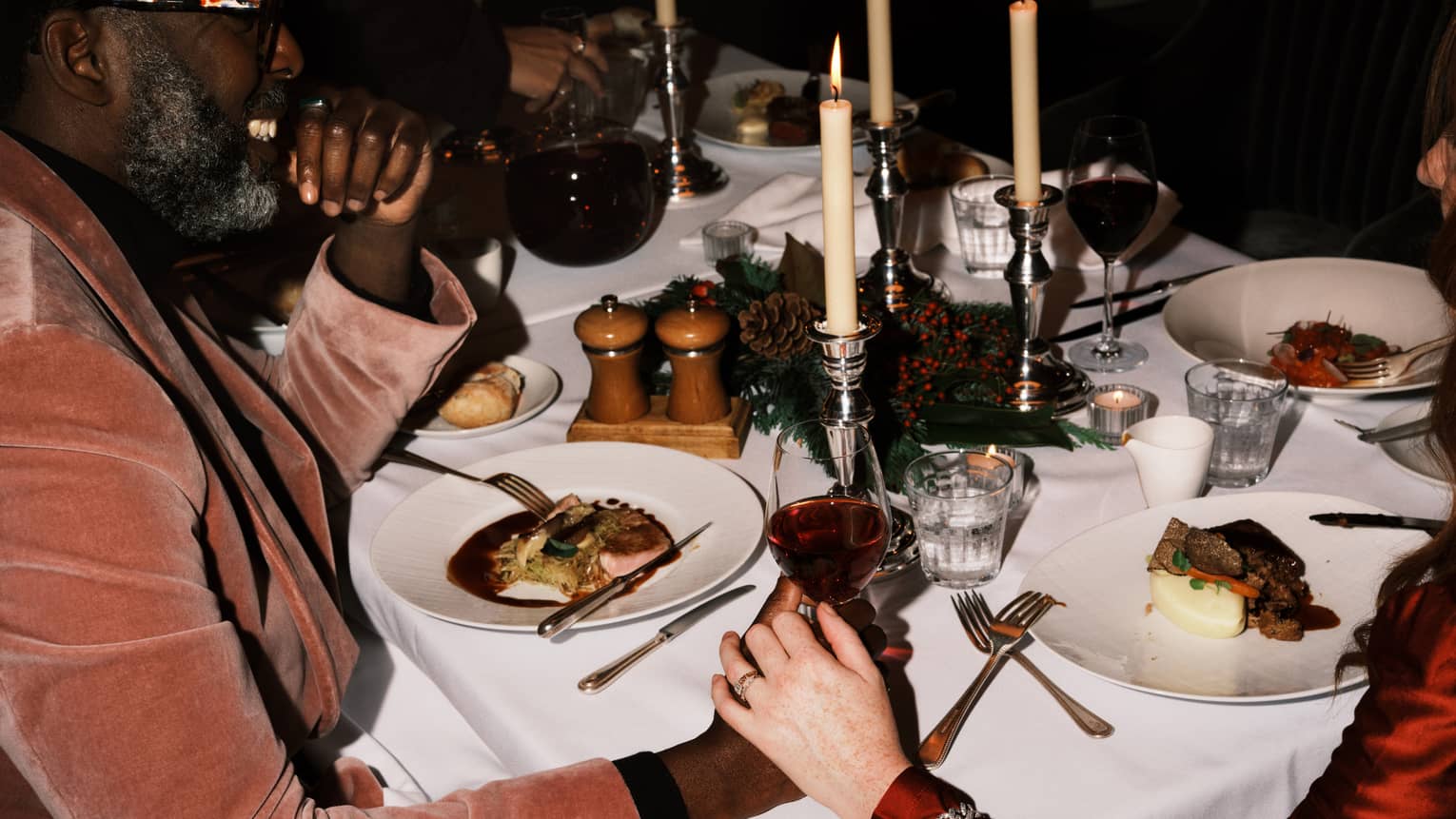 Two guests sitting at a dining table holding hands and a glass of wine.