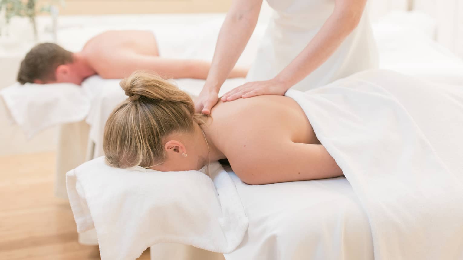 Couple laying on massage tables, spa staff massages woman's shoulders
