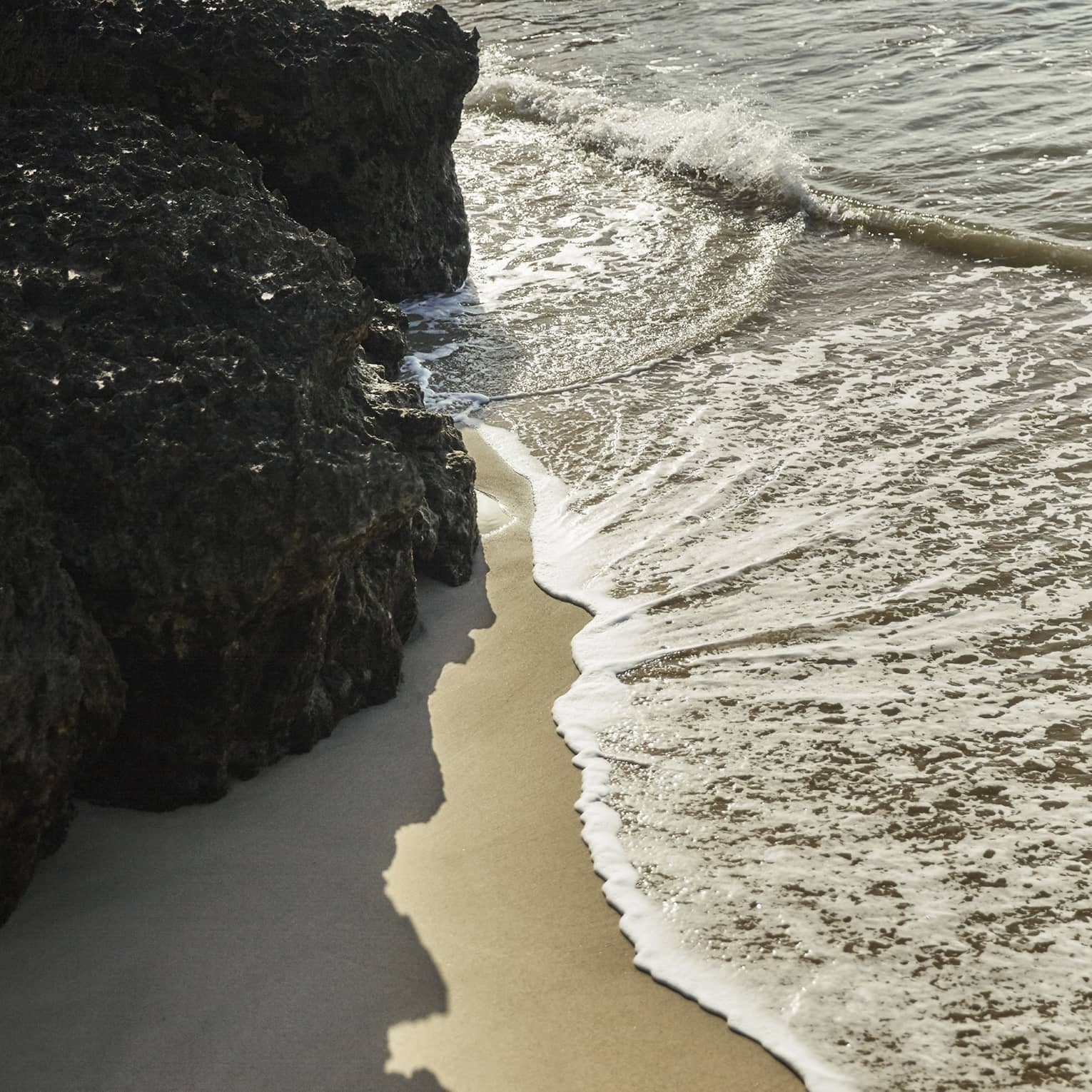 Calm waves brush up against a smooth beach and nearby rock