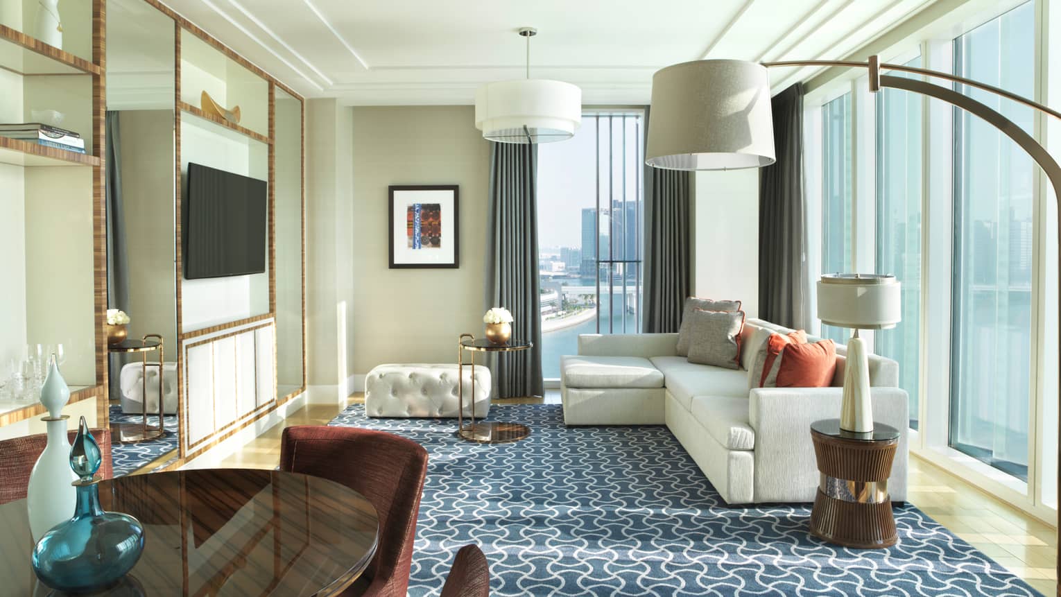 Sunny hotel room L-shaped white sofa in corner window, blue carpet, three lamps with large shades